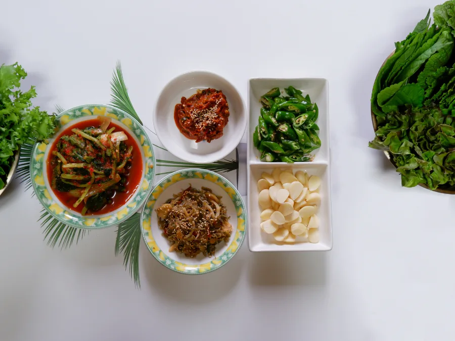 alt="Sliced garlic, sliced chili peppers, and assorted side dishes with lettuce wraps for Korean BBQ"
