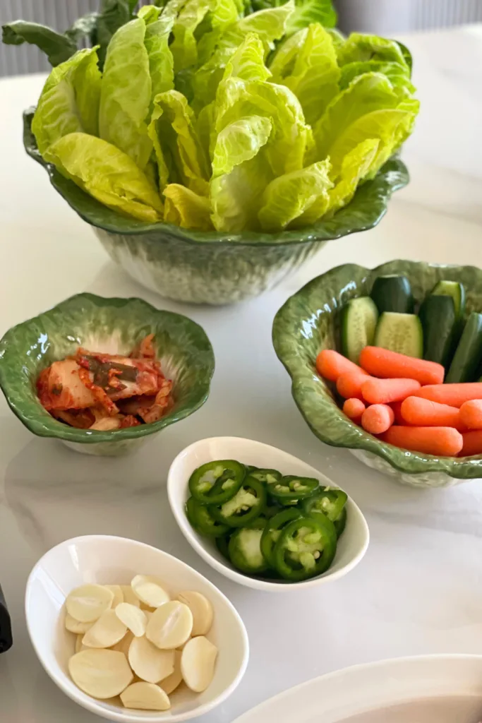 alt="Cabbage-shaped bowl set with lettuce wraps, kimchi, and vegetable sticks presented in a vertical arrangement"