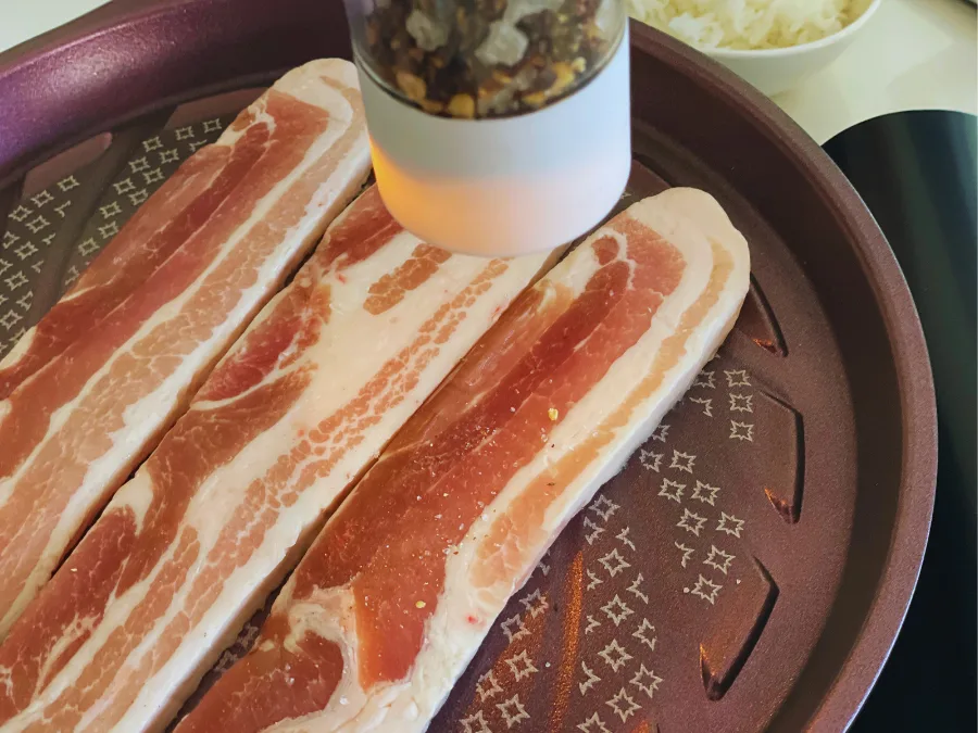 alt="Seasoning samgyeopsal with freshly ground salt and black pepper on a Techef grill pan"