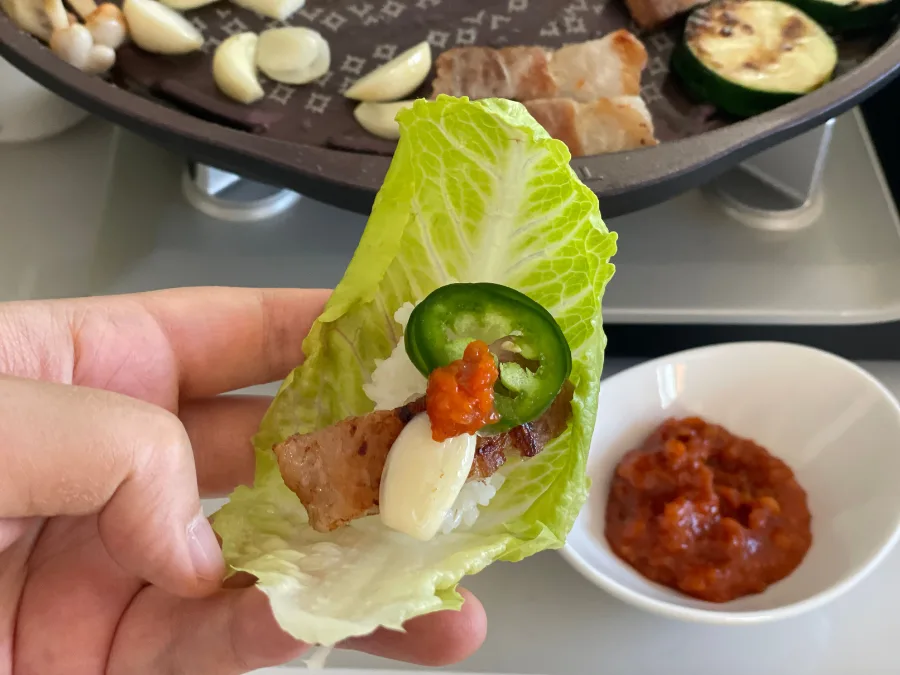 alt="Romaine lettuce wrap with grilled samgyeopsal, sliced garlic, jalapeño, and ssamjang"