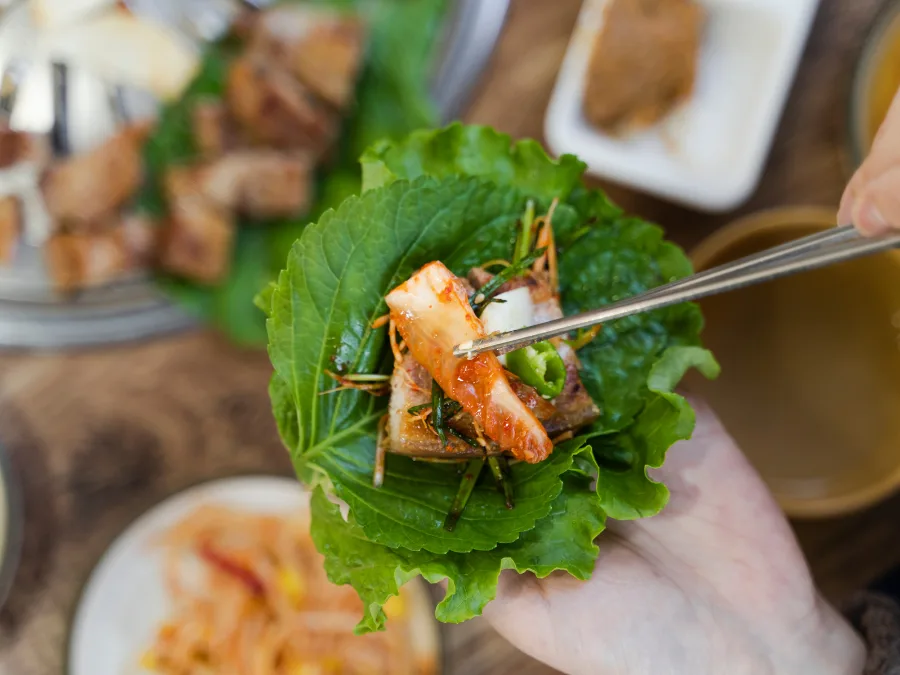 alt="Wrapping Korean BBQ with lettuce, perilla leaves, meat, green onion salad, chili, garlic, and kimchi"