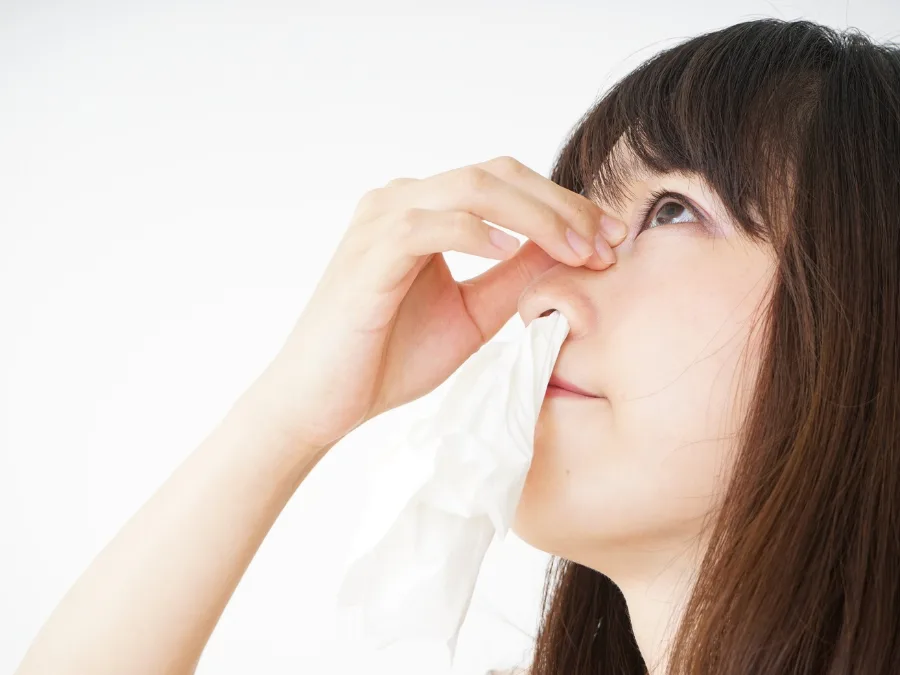 alt="Woman pinching her nose with a tissue"