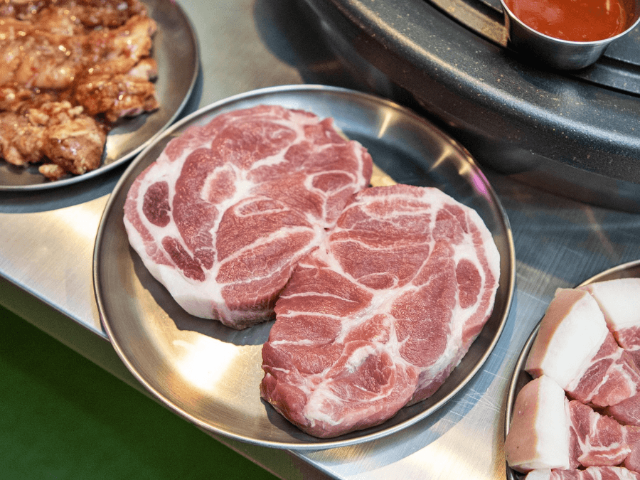 alt="Two pieces of pork neck (moksal) served on a stainless steel plate"  
