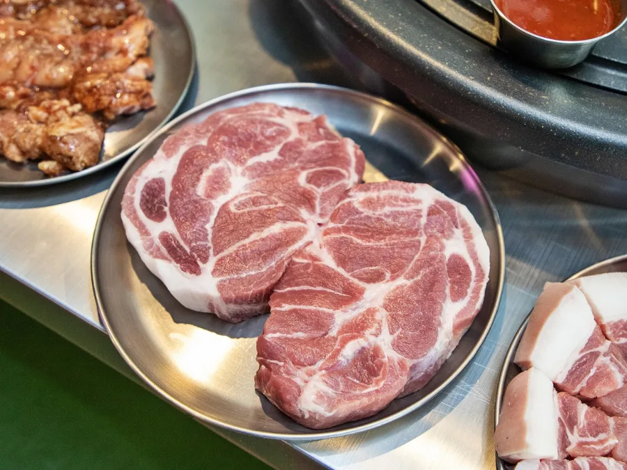 alt="Two pieces of pork neck (moksal) served on a stainless steel plate"
