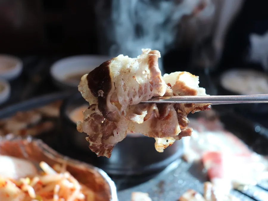alt="Chopsticks picking up a piece of grilled meat"
