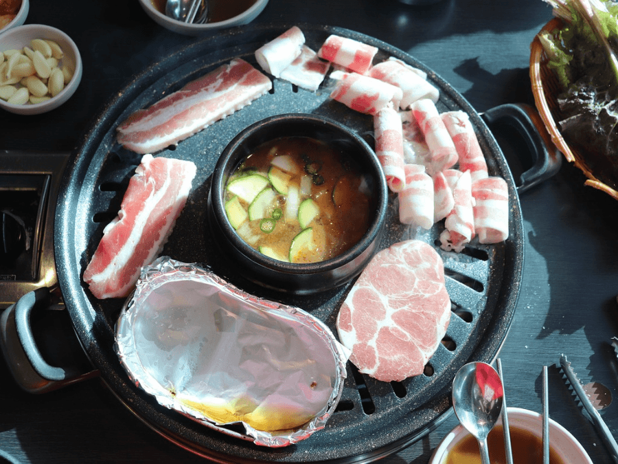 alt="Various types of meat on a Korean BBQ grill with soybean paste stew (doenjang jjigae) simmering in the center"  
