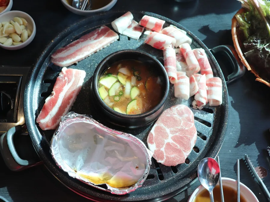 alt="Various types of meat on a Korean BBQ grill with soybean paste stew (doenjang jjigae) simmering in the center"
