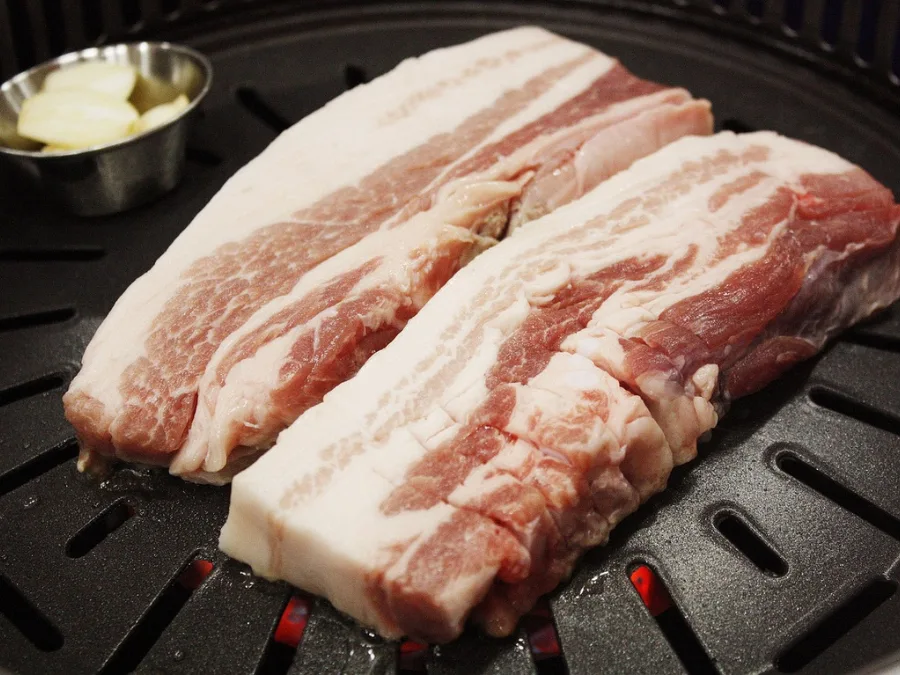 alt="Pork belly placed on the grill for Korean BBQ"
