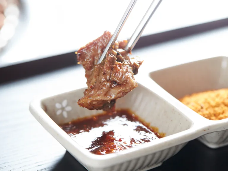 alt="A piece of grilled Korean BBQ meat dipped in ssamjang sauce"