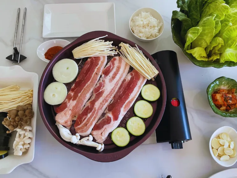 alt="Korean BBQ table setting with grilled samgyeopsal, dipping sauces, and side dishes"
