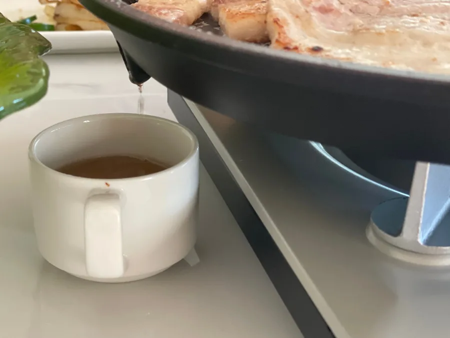 alt="Rendered pork belly fat dripping through the grease drain while grilling samgyeopsal (pork belly)"